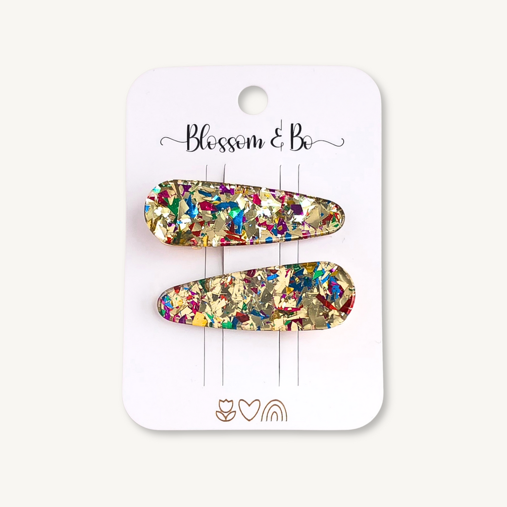 Two gold-toned hair claw clips filled with multicolor glitter, displayed on a white card labeled 'Blossom & Bo'.
