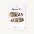 Two gold-toned hair claw clips filled with multicolor glitter, displayed on a white card labeled 'Blossom & Bo'.
