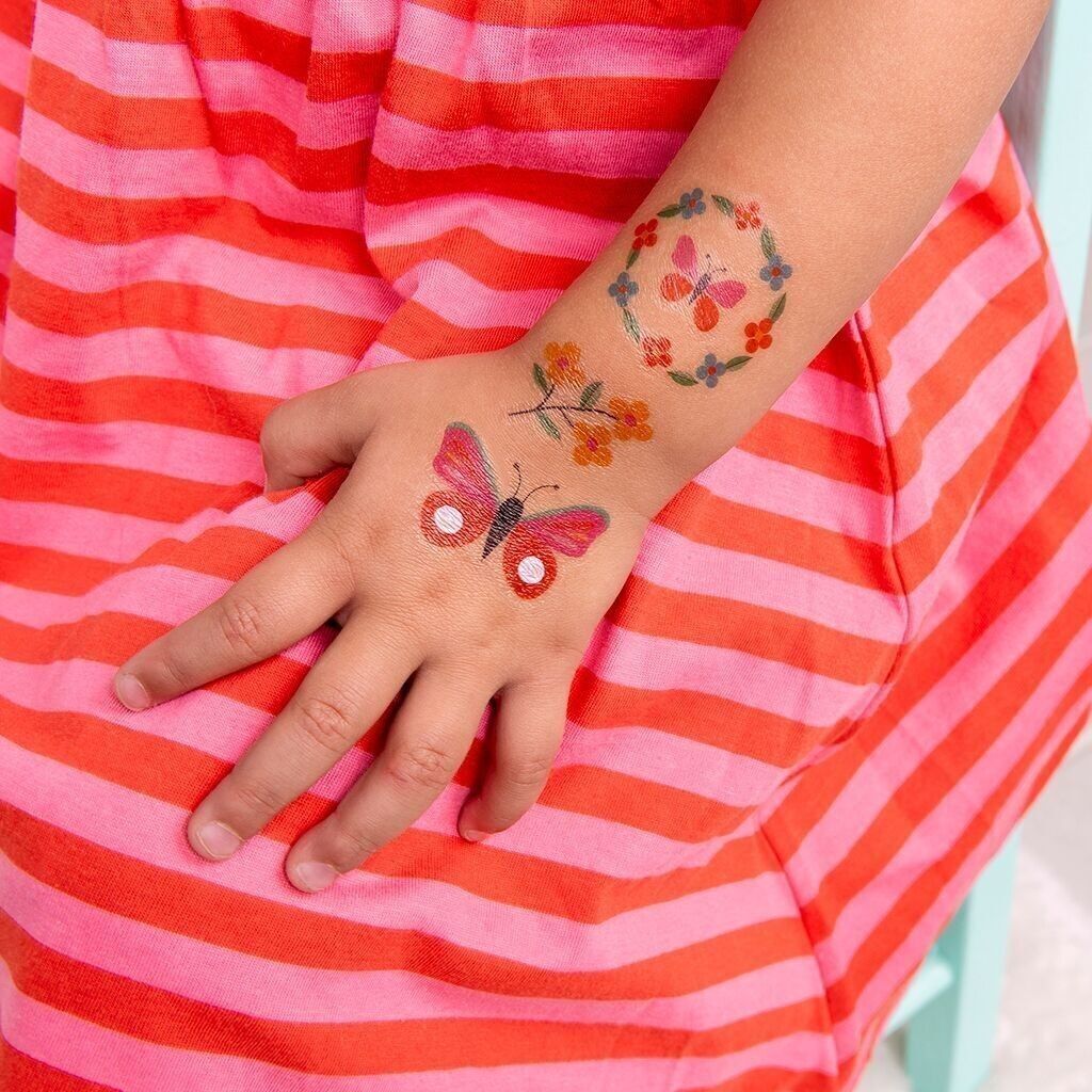 Person wearing colorful temporary tattoos on a red and pink striped shirt.