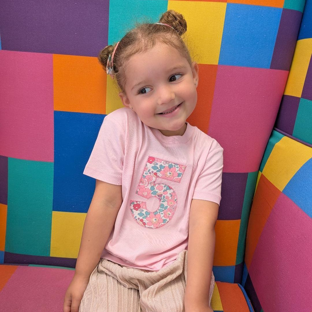 A little girl wearing a pink t-shirt with a fabric number 5 on the front.