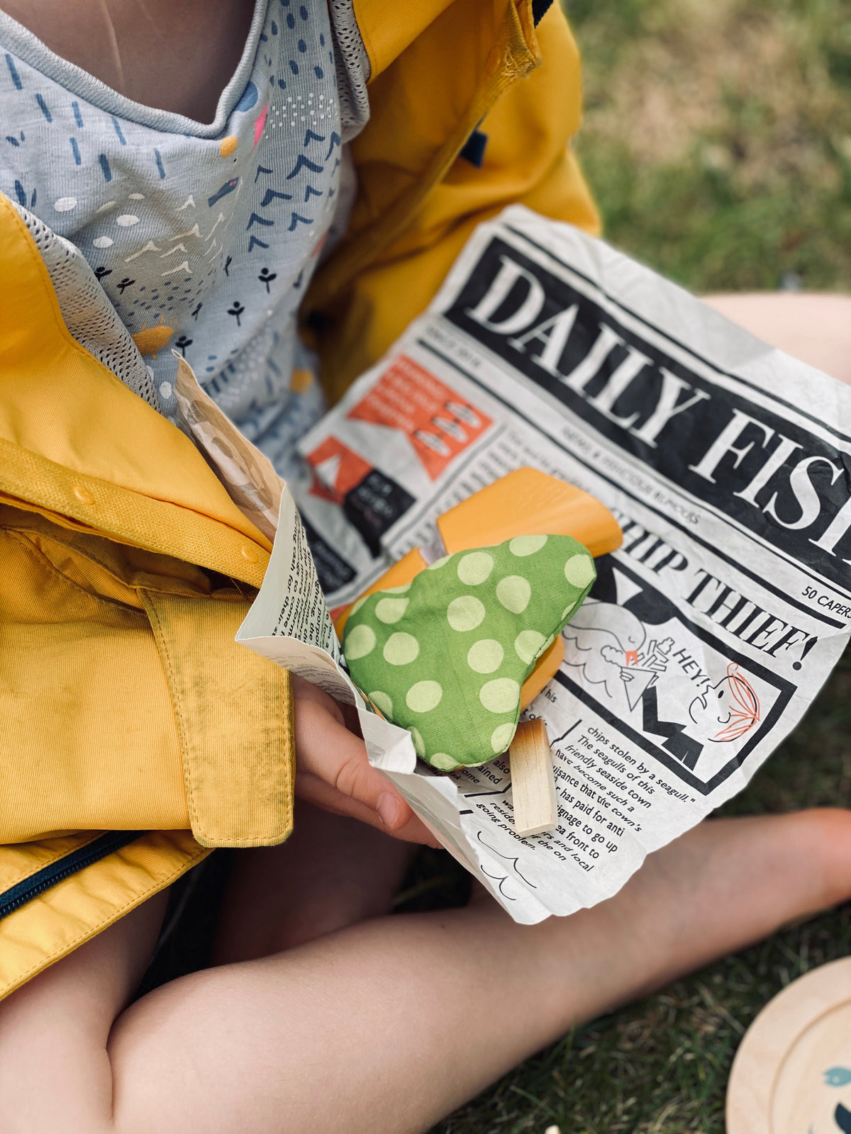 Child holding a piece of newspaper with retend peas, fish and chips