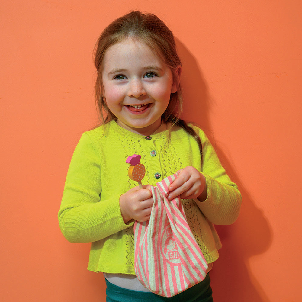 Young girl in a bright yellow sweater holding a pink and white striped bag against an orange background