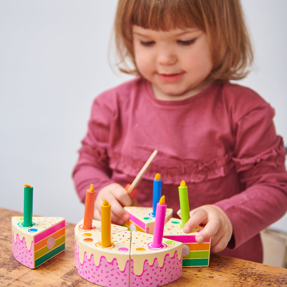 Child playing with a colorful wooden toy birthday cake on a wooden table.