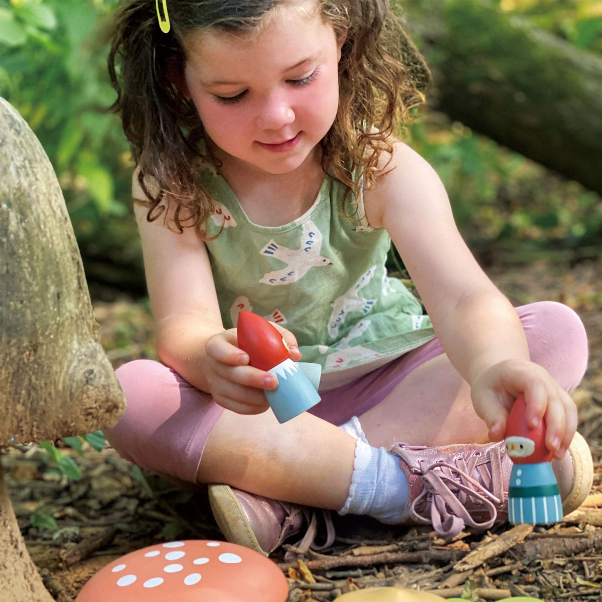Child sitting in a forest playing with the little wooden gnome set amongst the wooden mushrooms and leaves