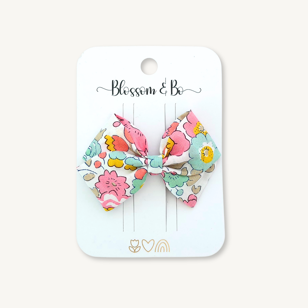 A floral fabric hair bow attached to a white card labeled 'Blossom & Bo', photographed against a light beige background.