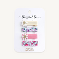 A set of four hair clips on a white display card labeled 'Blossom & Bo'. The clips include cream, floral prints, and solid pink ribbons, with two decorated with white daisy flowers and gold centers.