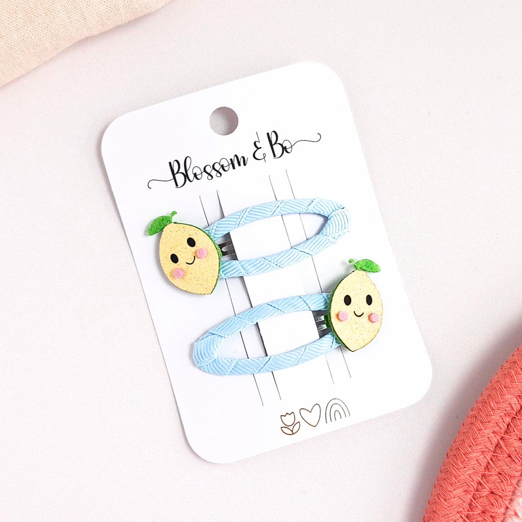 Set of two blue ribbon lined snap clips with smiley yellow lemon faces.
