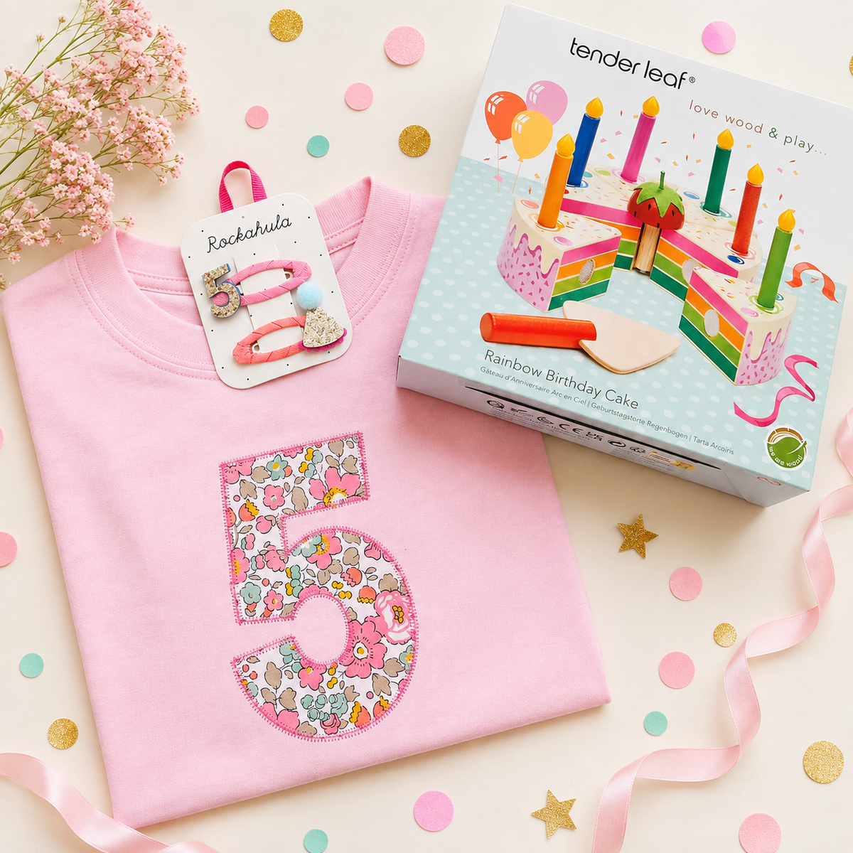 A pink crewneck t-shirt with a large floral-patterned number 5 on the front, displayed next to its 'tender leaf' Rainbow Birthday Cake playset box on a decorated pastel background.