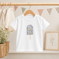 White t-shirt on a hanging rail with an ice lolly applique on the front in purple Betsy Liberty of London fabric.